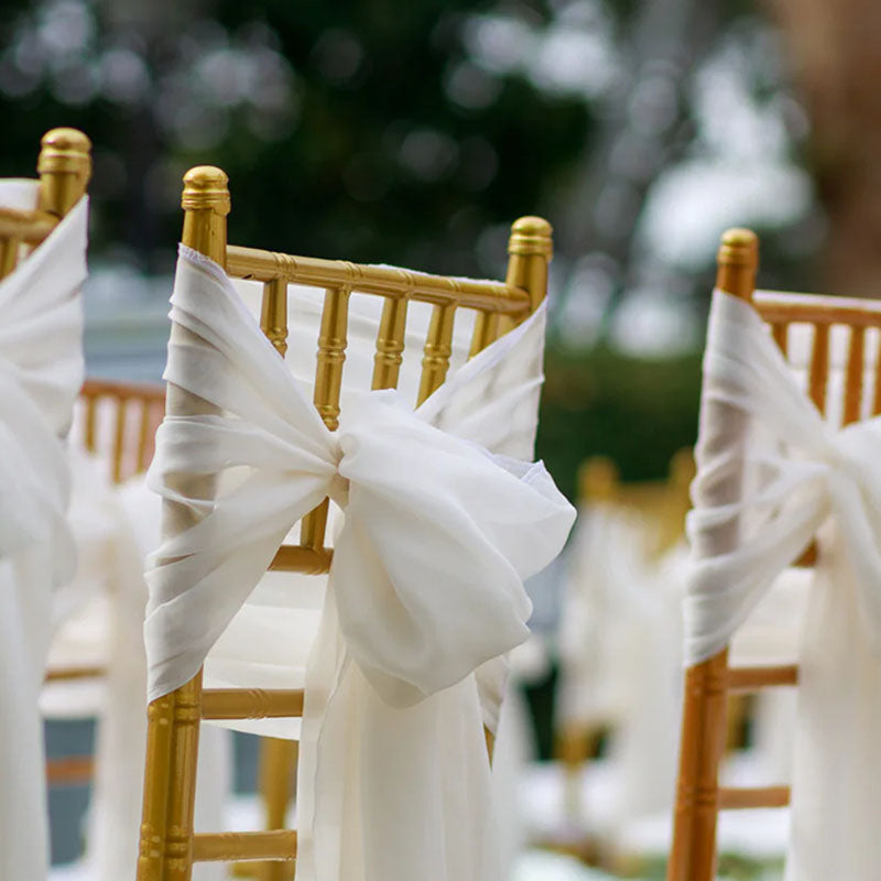 Decorative chairs with white ribbons at an outdoor event.